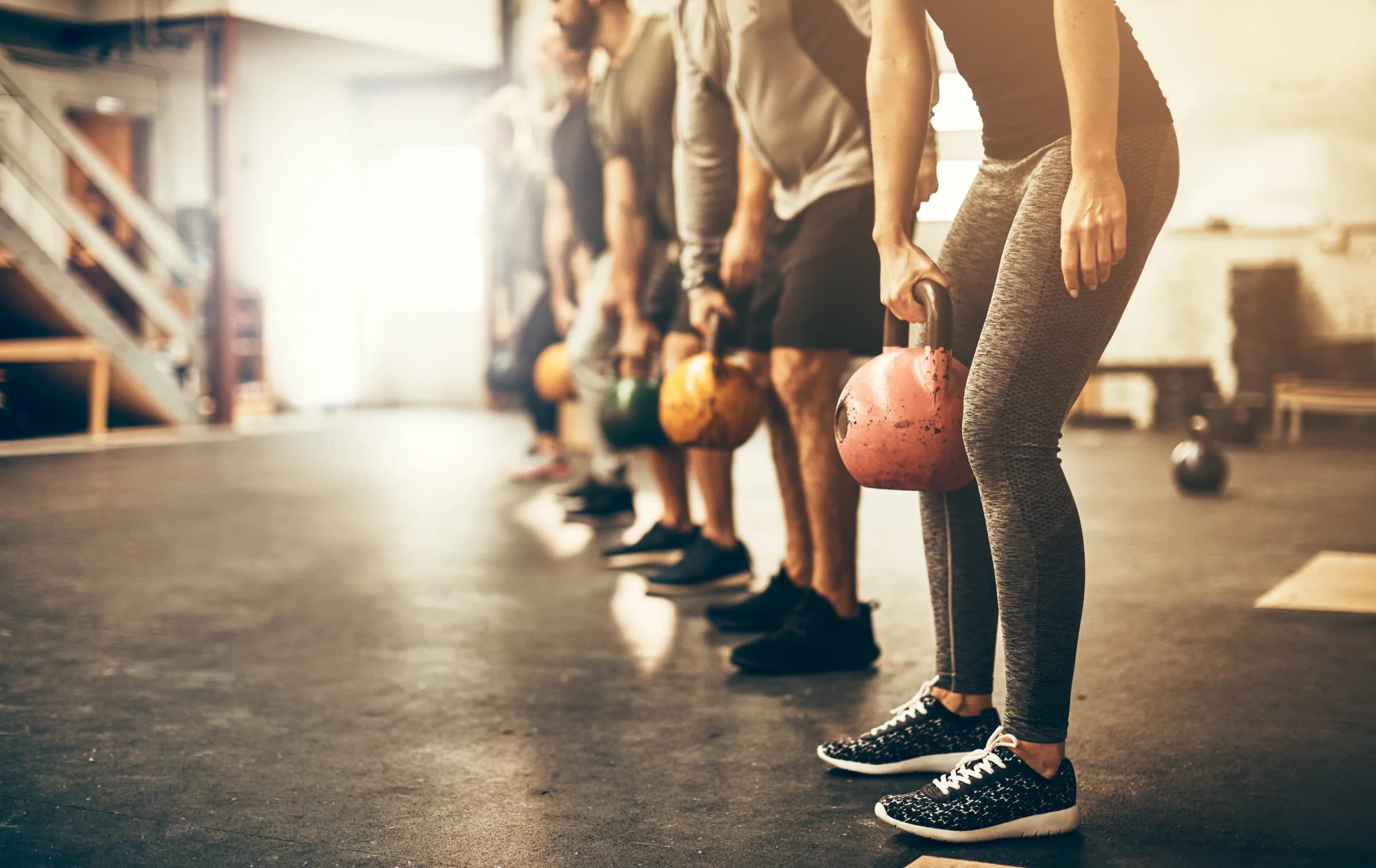 A line of people training together with kettlebells, guided by a coach